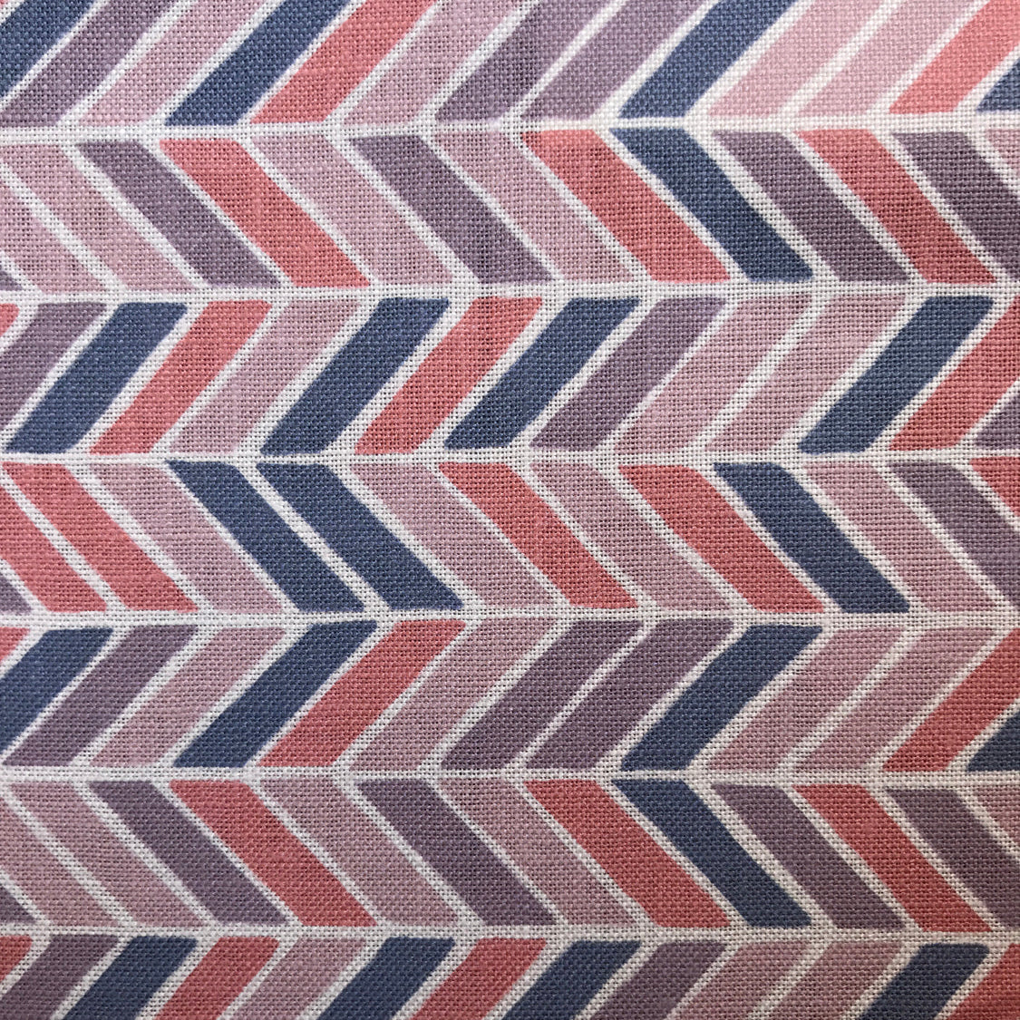 Detail of fabric in a geometric herringbone print in coral, purple and navy on a white field.