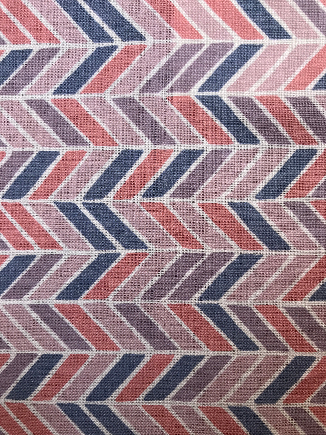 Detail of fabric in a geometric herringbone print in coral, purple and navy on a white field.