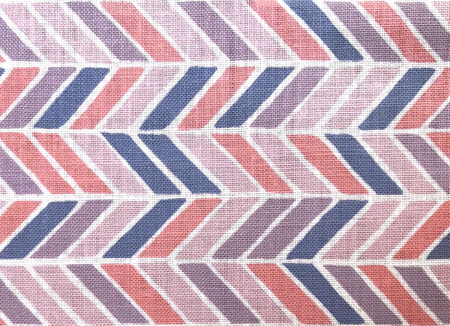 Detail of fabric in a geometric herringbone print in coral, purple and navy on a white field.