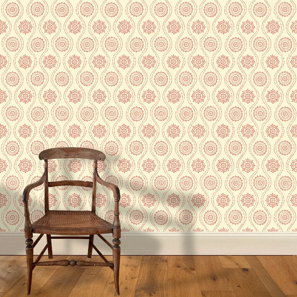 A wooden chair stands in front of a wall papered in a playful floral stripe in pink on a cream field.