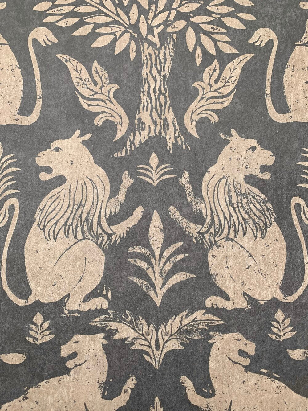 Close-up of wallpaper in a lion and plant print in cream on a mottled gray field.