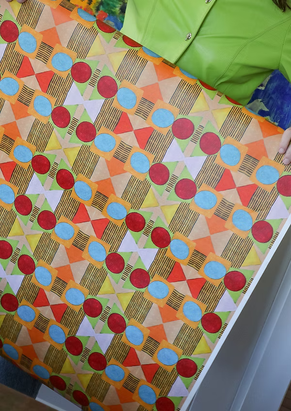 Detail of a woman holding a wallpaper with a collaged circle, square and diamond stripe wallpaper in red, orange, green and pink. 