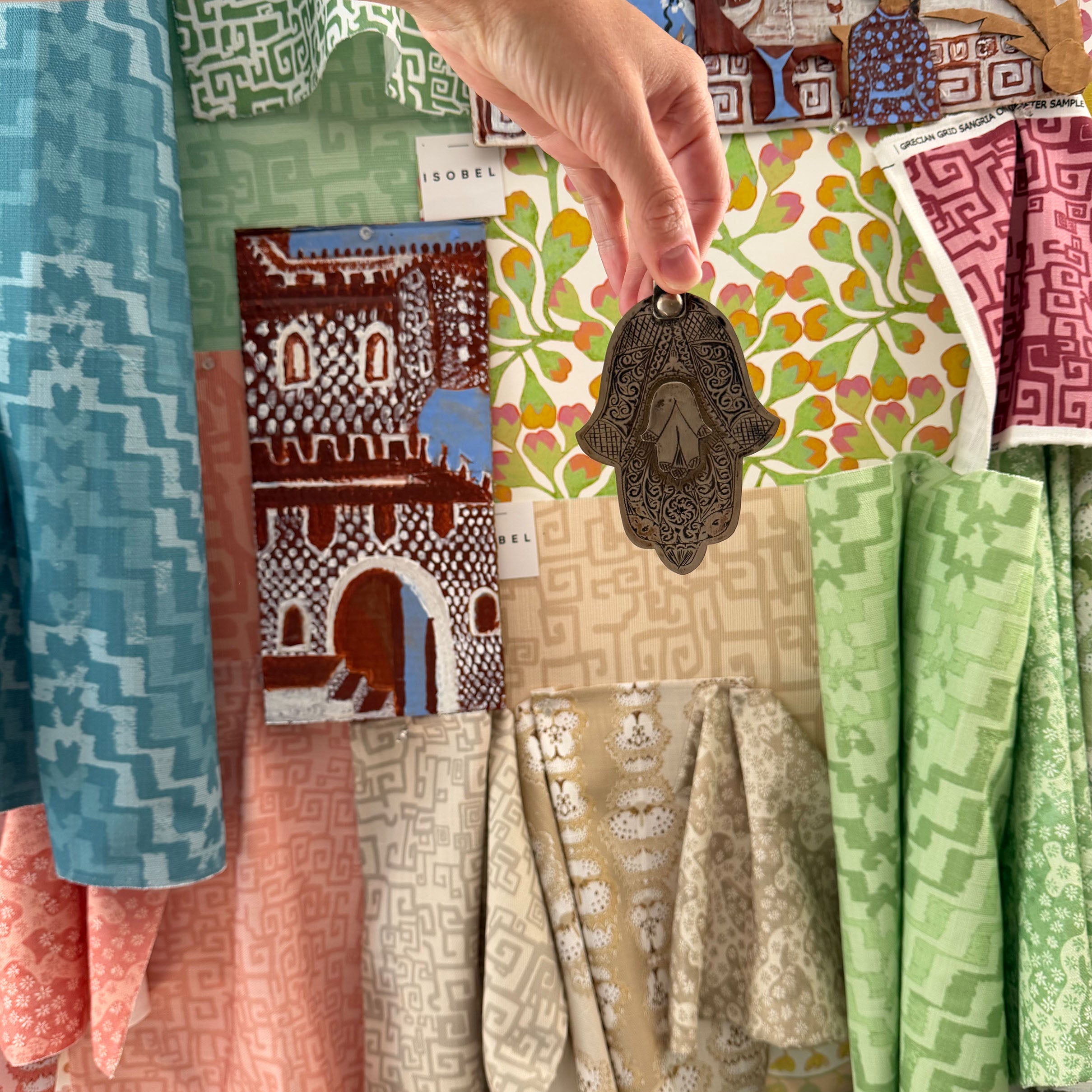 Moodboard with brightly colored fabric swatches and woman's arm holding an ornate metal charm. 