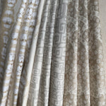 Stack of folded fabric swatches in various patterns in a soft neutral palette. 