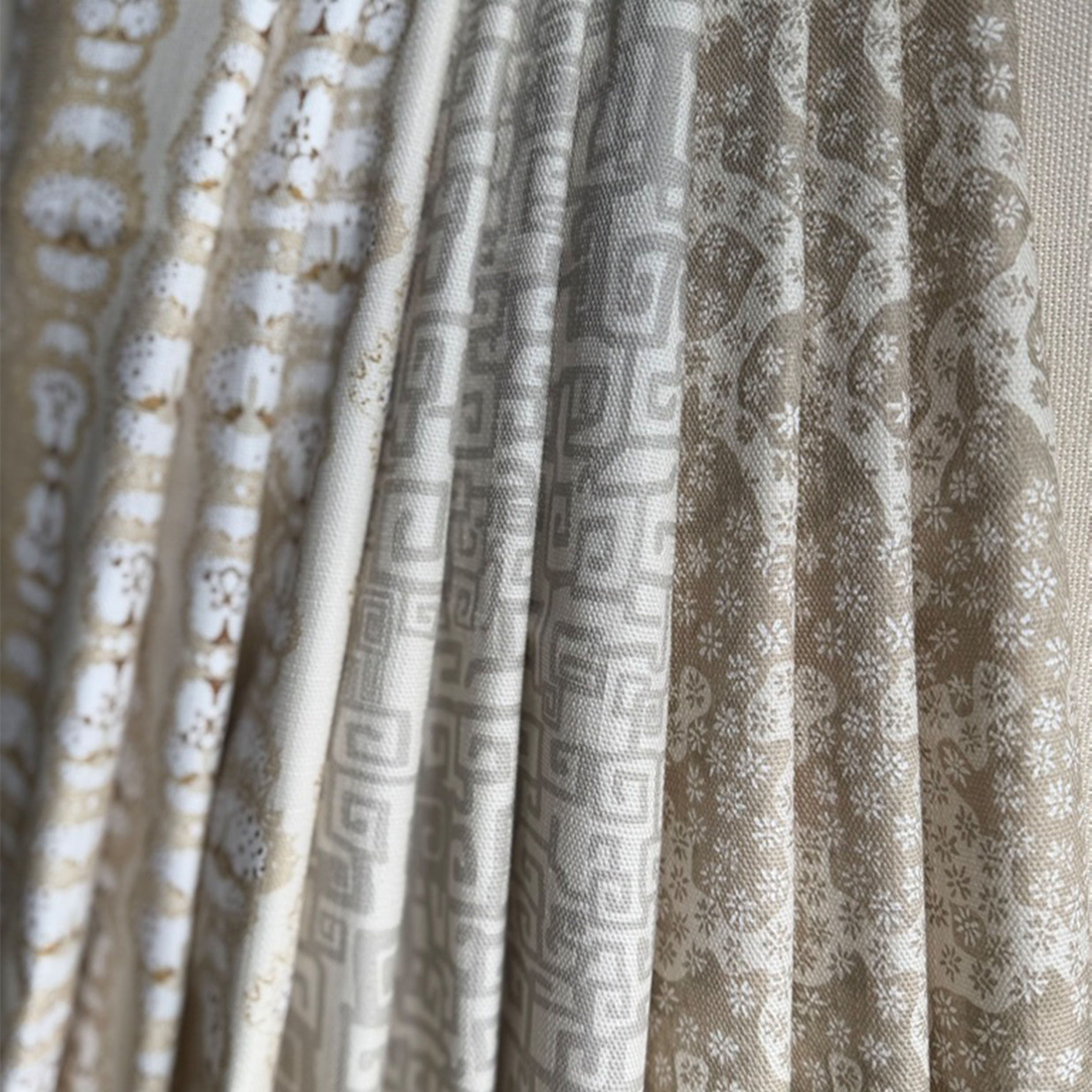 Stack of folded fabric swatches in various patterns in a soft neutral palette. 