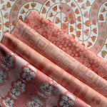 Stack of folded fabric swatches in various patterns in a soft pink palette. 