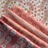 Stack of folded fabric swatches in various patterns in a soft pink palette. 