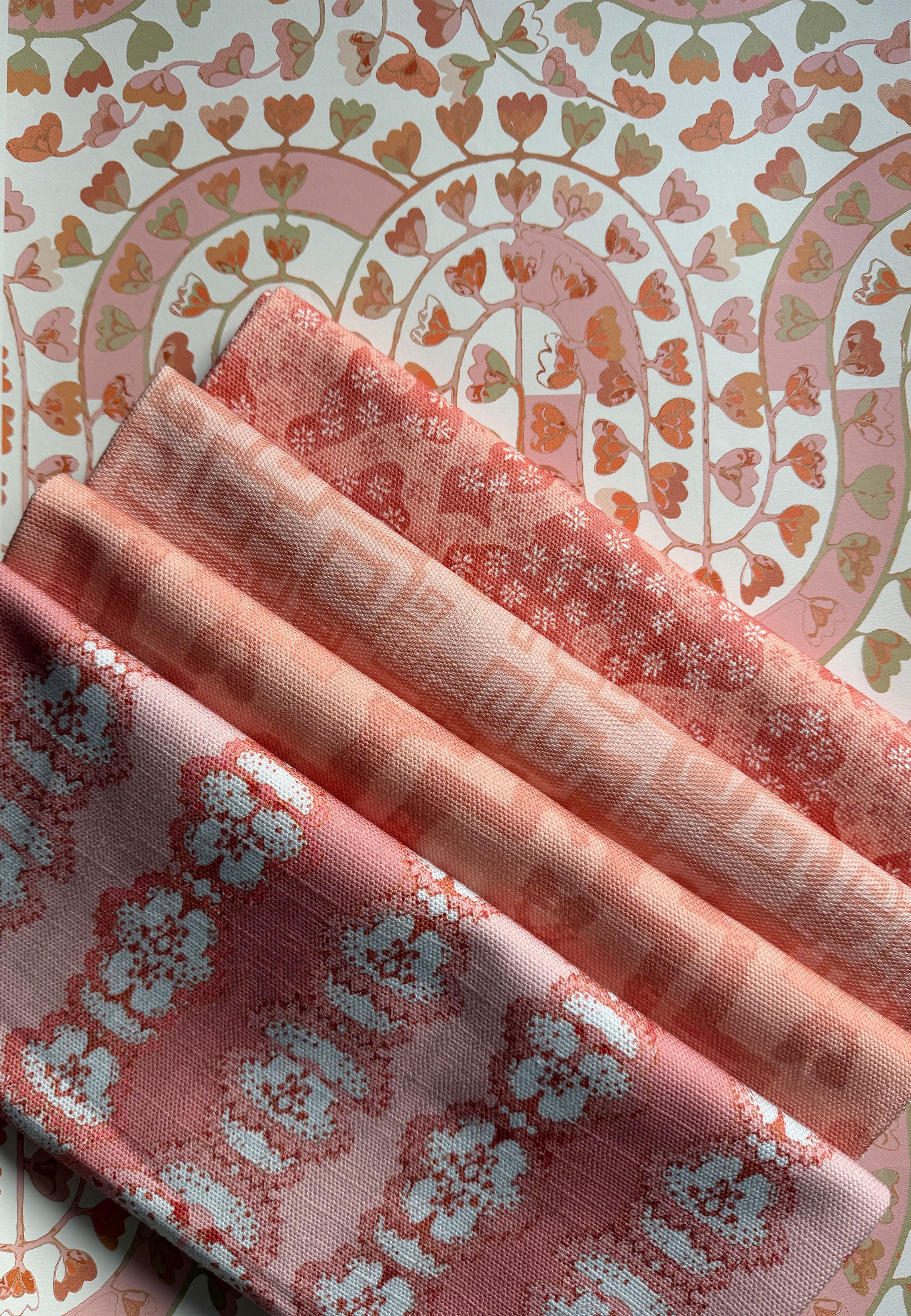 Stack of folded fabric swatches in various patterns in a soft pink palette. 