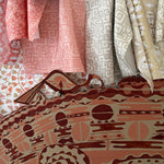 Draped fabric swatches in pink, beige and green against a hand painted screen.