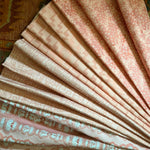 Stack of folded fabric swatches in various patterns in pink on an antique carpet.