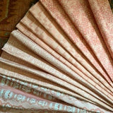 Stack of folded fabric swatches in various patterns in pink on an antique carpet.