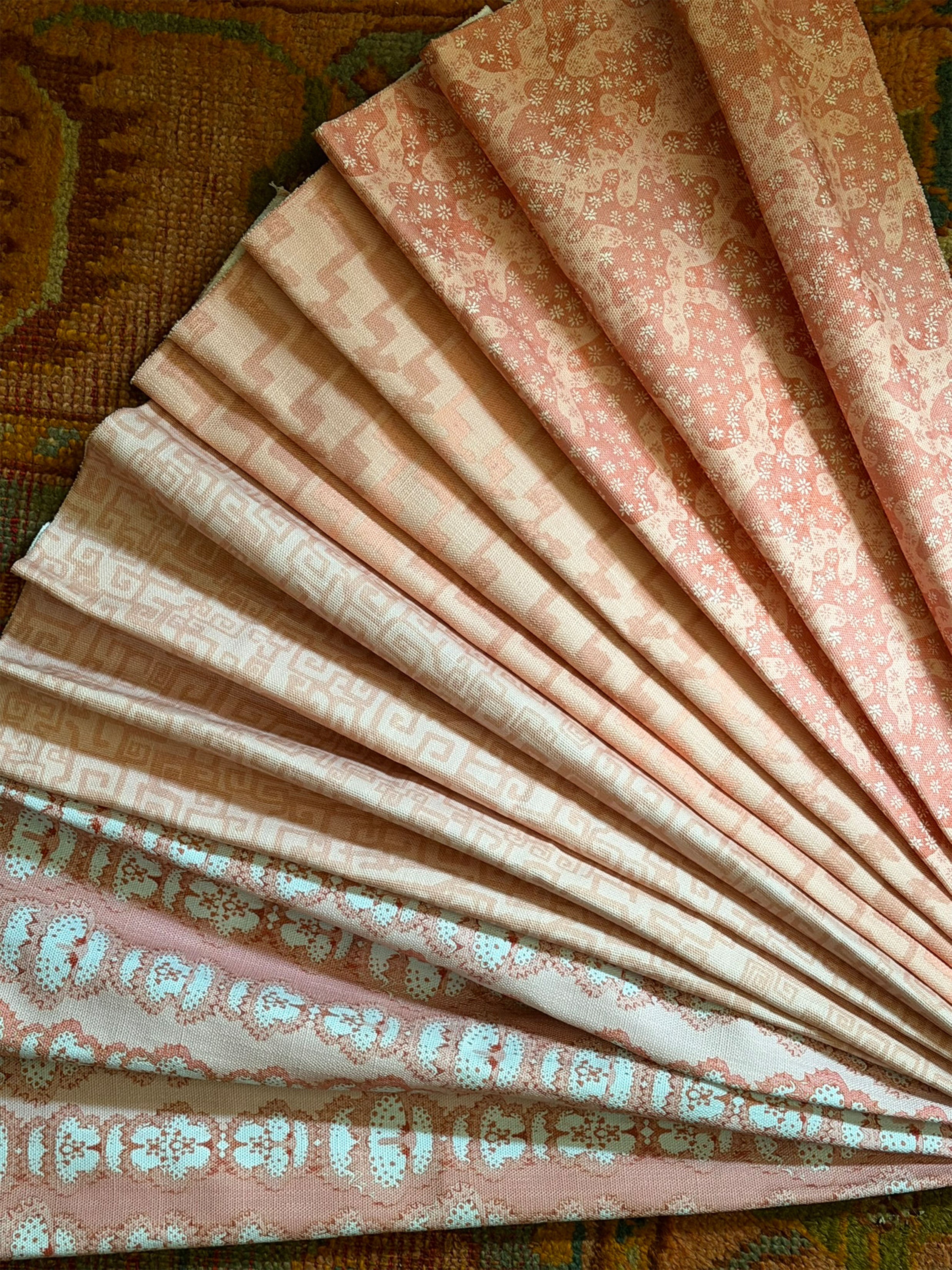Stack of folded fabric swatches in various patterns in pink on an antique carpet.