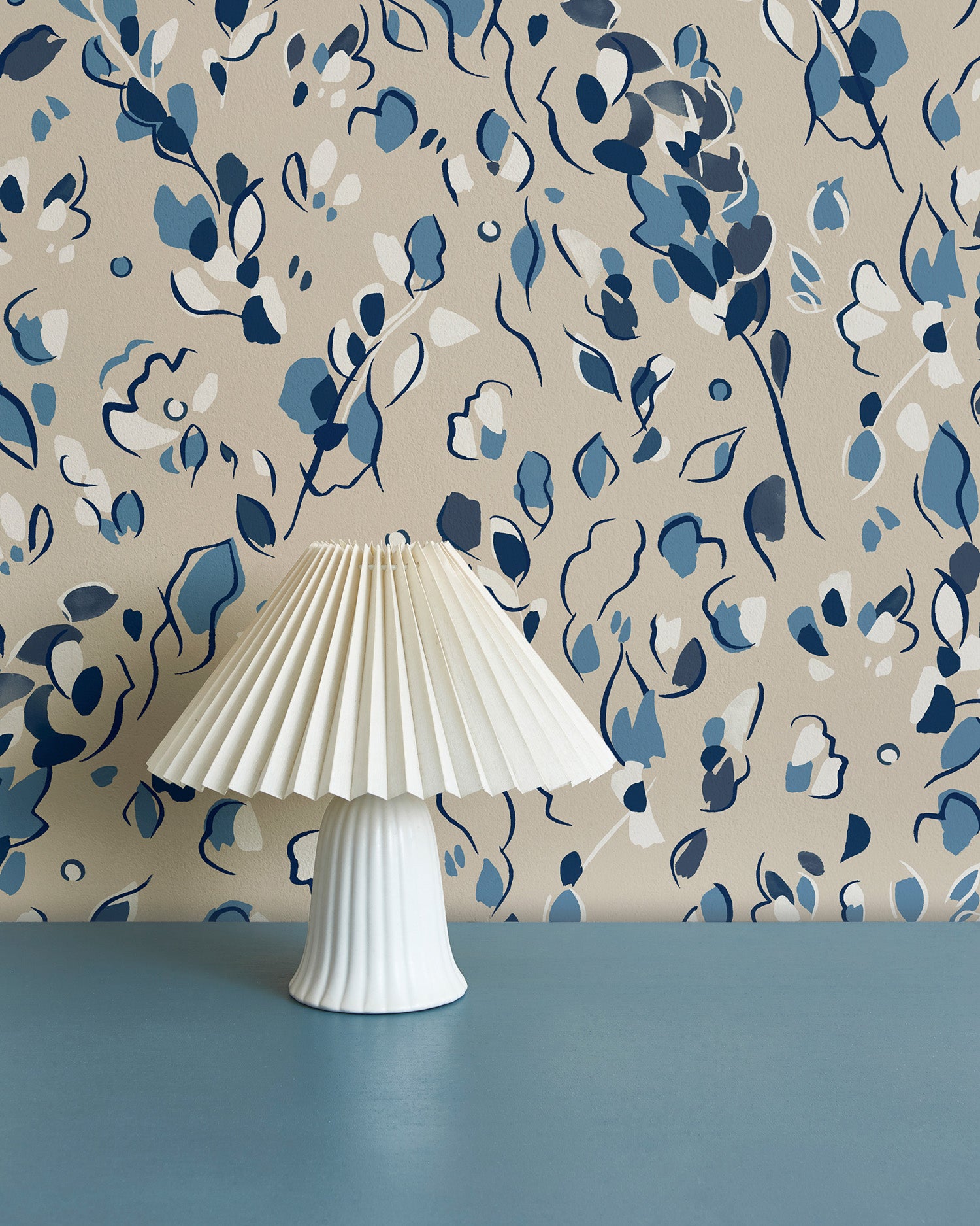 Modernist lamp in front of a wall papered in a painterly leaf print in shades of blue, white and tan.