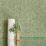 Two vases stand in front of a wall papered in a minimalist floral print in sage on a green field.