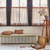 An artists studio interior with a paint kit, brushes and artwork scattered on the floor against a wall of windows with  sheer blush colored curtains in blush pink.