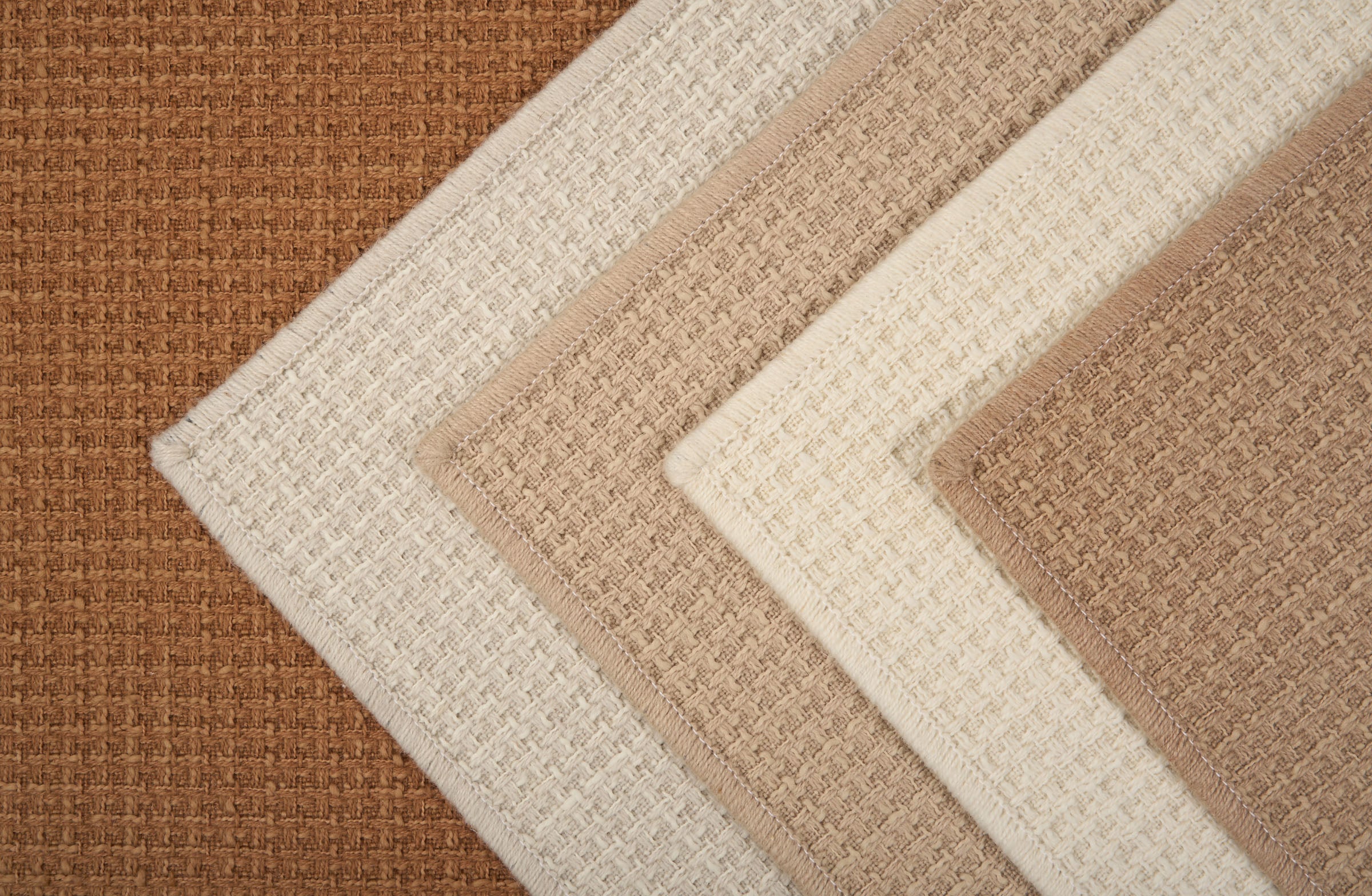 Stack of broadloom carpets in neutral colors. 