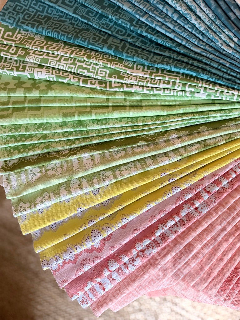 Stack of folded fabric swatches in various patterns in blue, green, yellow and pink.