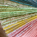 Stack of folded fabric swatches in various patterns in blue, green, yellow and pink.