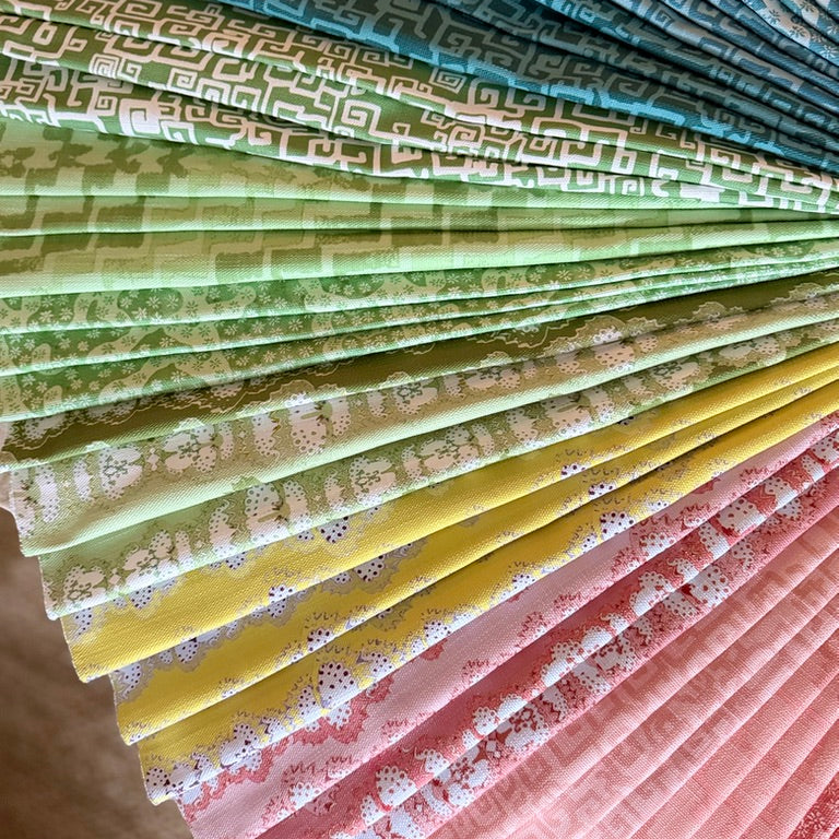 Stack of folded fabric swatches in various patterns in blue, green, yellow and pink.