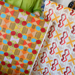Cropped image of two figured holding large pieces of geometric wallpapers in bright orange, red, yellow and white. 