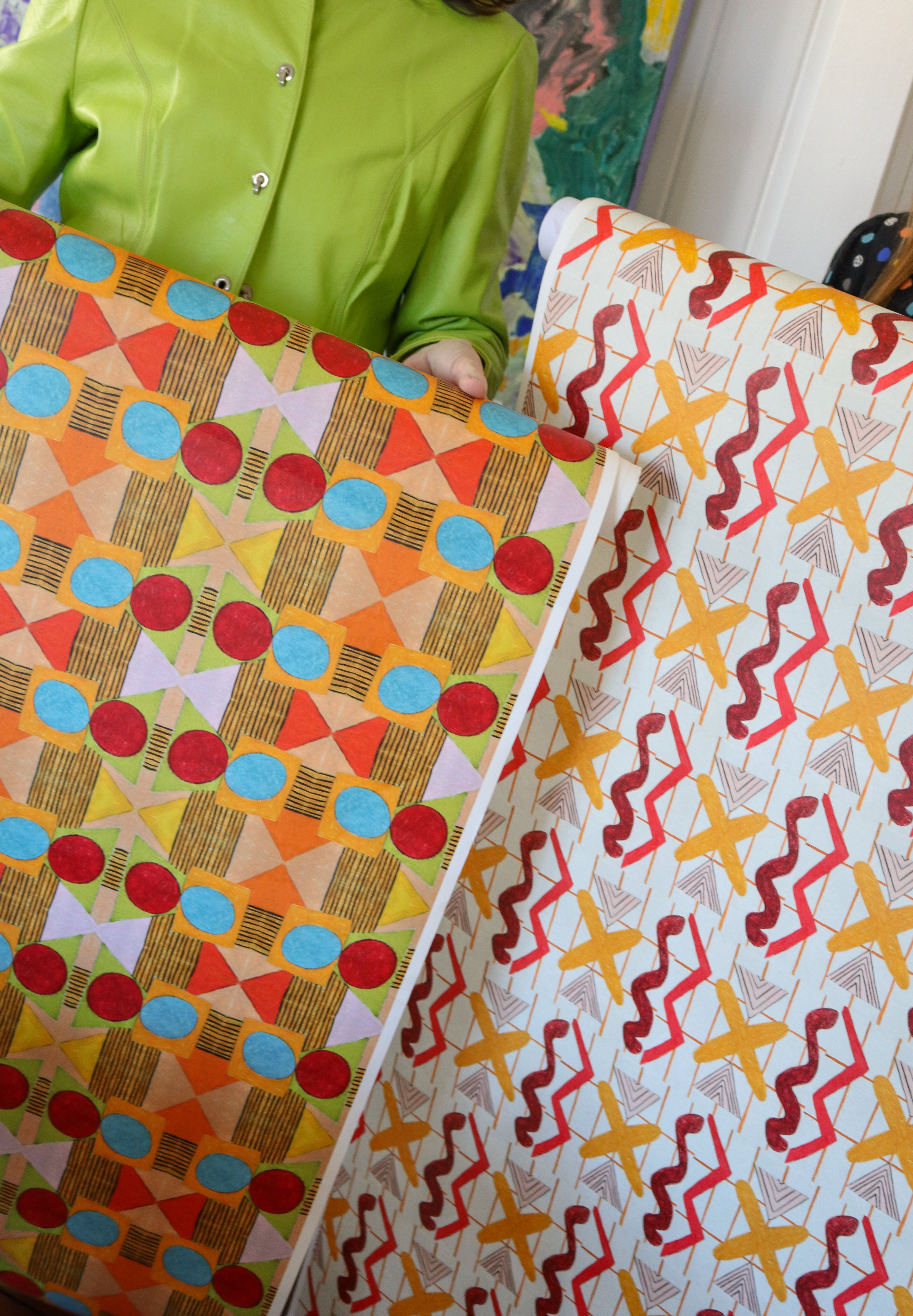Cropped image of two figured holding large pieces of geometric wallpapers in bright orange, red, yellow and white. 