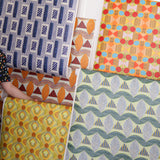 Detail image of various bold geometric wallpapers taped to a white wall with crown molding. 