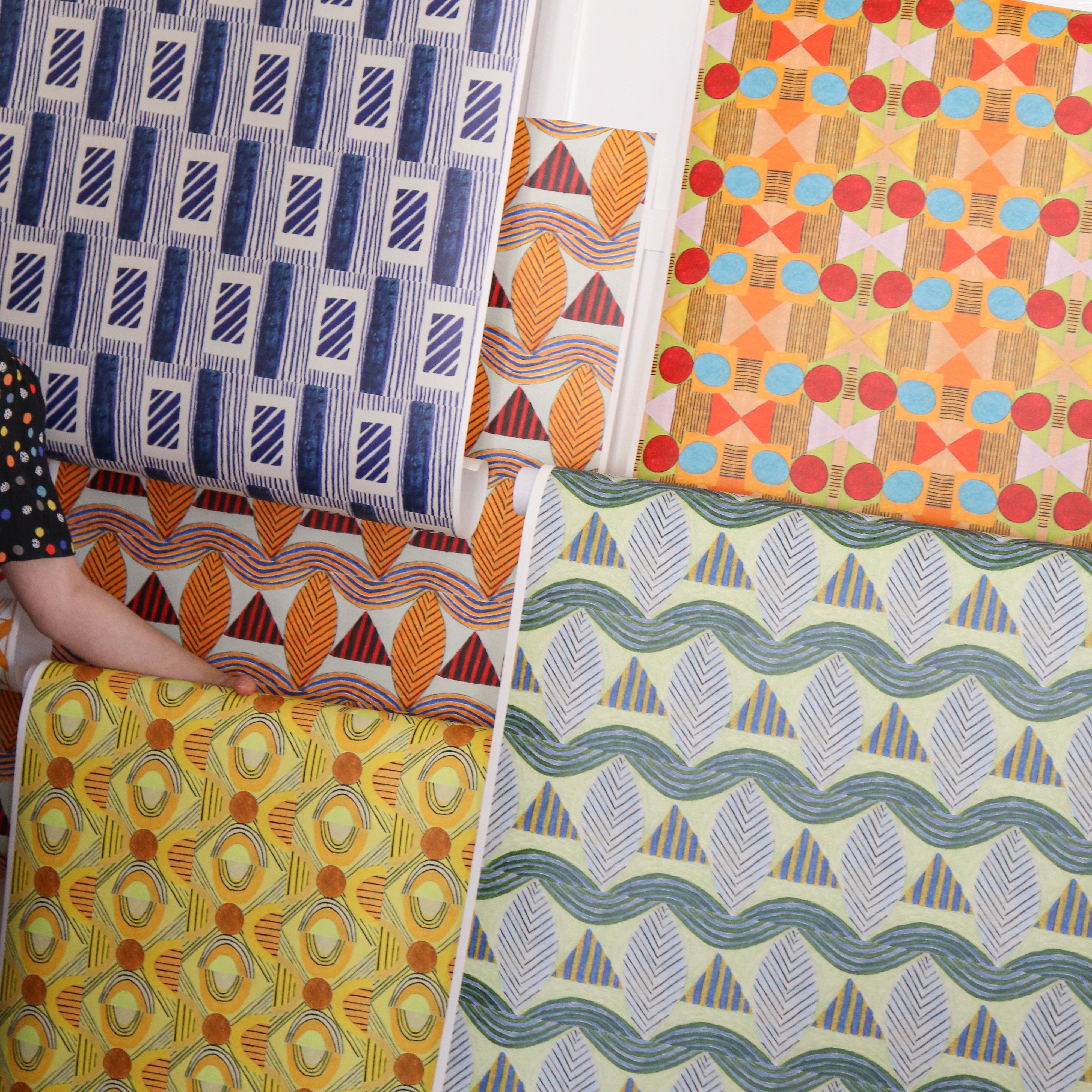 Detail image of various bold geometric wallpapers taped to a white wall with crown molding. 