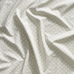 Close up of gently draped printed linen with dense floral medallion pattern in white on beige.