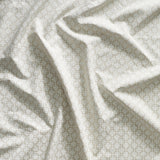 Close up of gently draped printed linen with dense floral medallion pattern in white on beige.