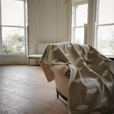Room with a embroidered linen panel with white lips draped over a chair, large windows allowing natural light.