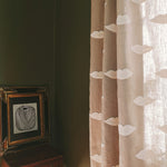 Linen curtain with white lip embroidery in a room with a wooden table and framed artwork.
