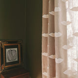 Linen curtain with white lip embroidery in a room with a wooden table and framed artwork.