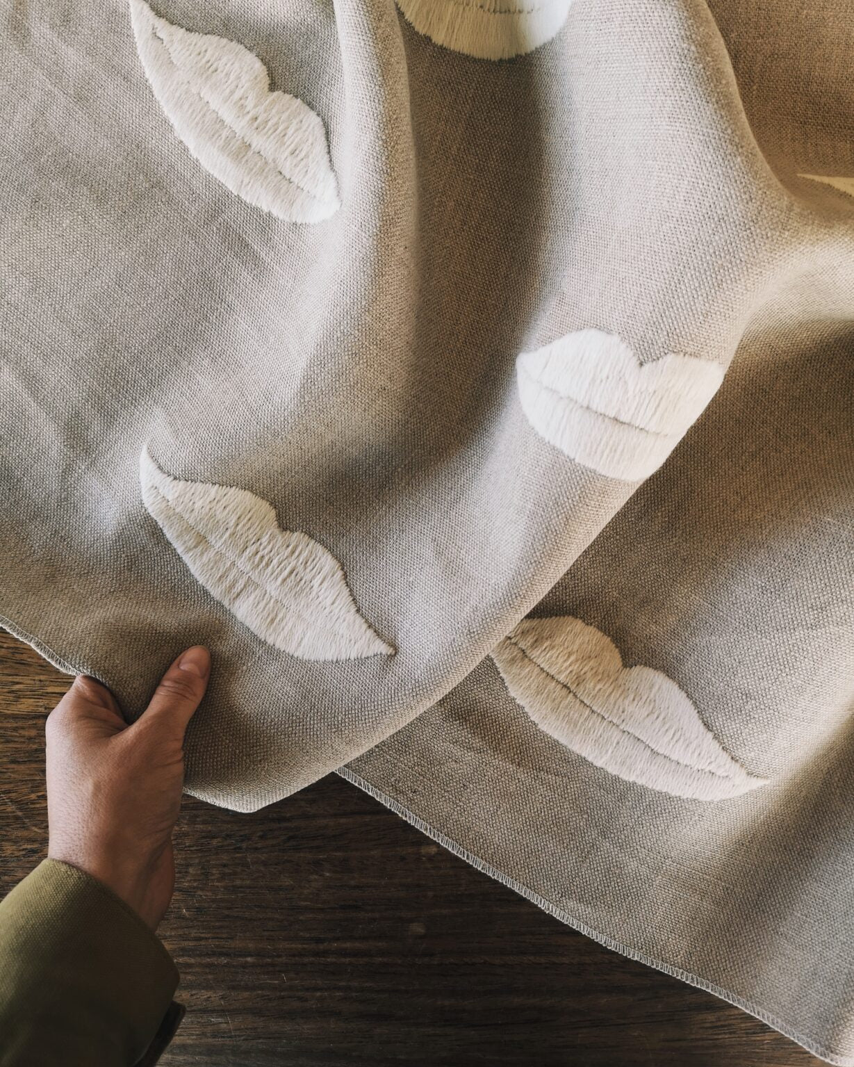 Linen with white embroidered lip pattern held by a hand on a wooden surface