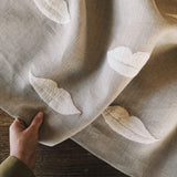 Linen with white embroidered lip pattern held by a hand on a wooden surface