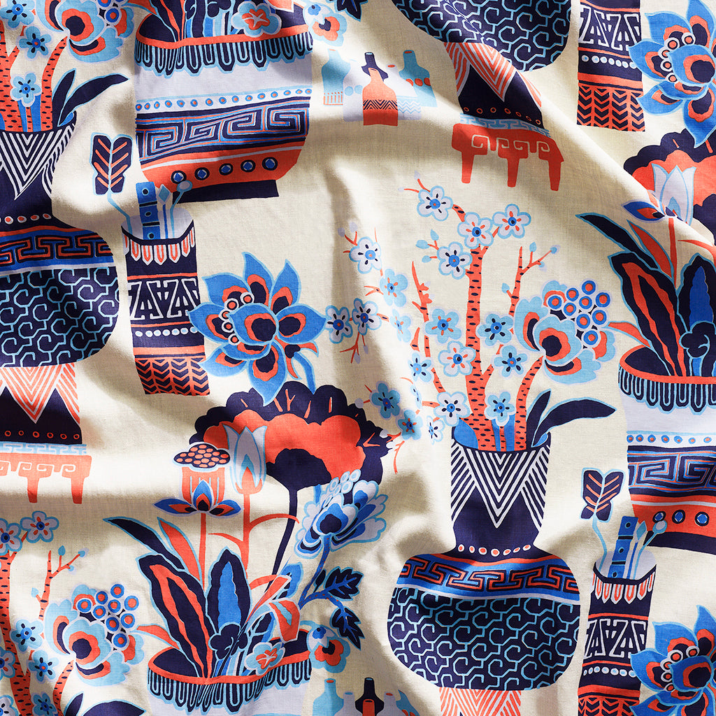 Close up of gently draped fabric in an ornate hand drawn urn and floral pattern in coral and blue on white. 