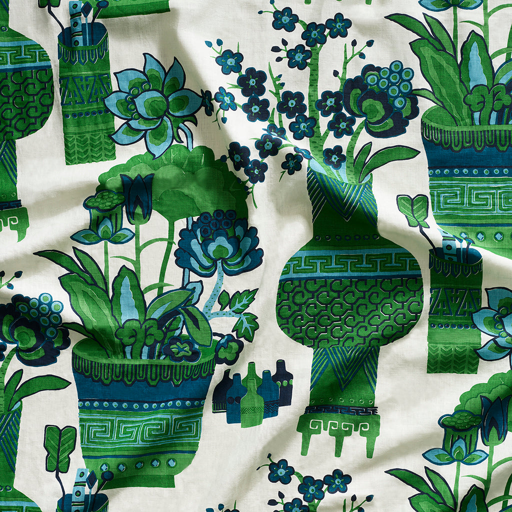 Close up of gently draped fabric in an ornate hand drawn urn and floral pattern in green and blue on white. 