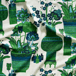 Close up of gently draped fabric in an ornate hand drawn urn and floral pattern in green and blue on white. 