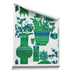 Roll of wallpaper in an ornate hand drawn urn and floral pattern in green and blue on white. 