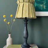 An end table with flowers, a stack of books and a lamp with a shade upholstered in a scrolling stem and leaf print.