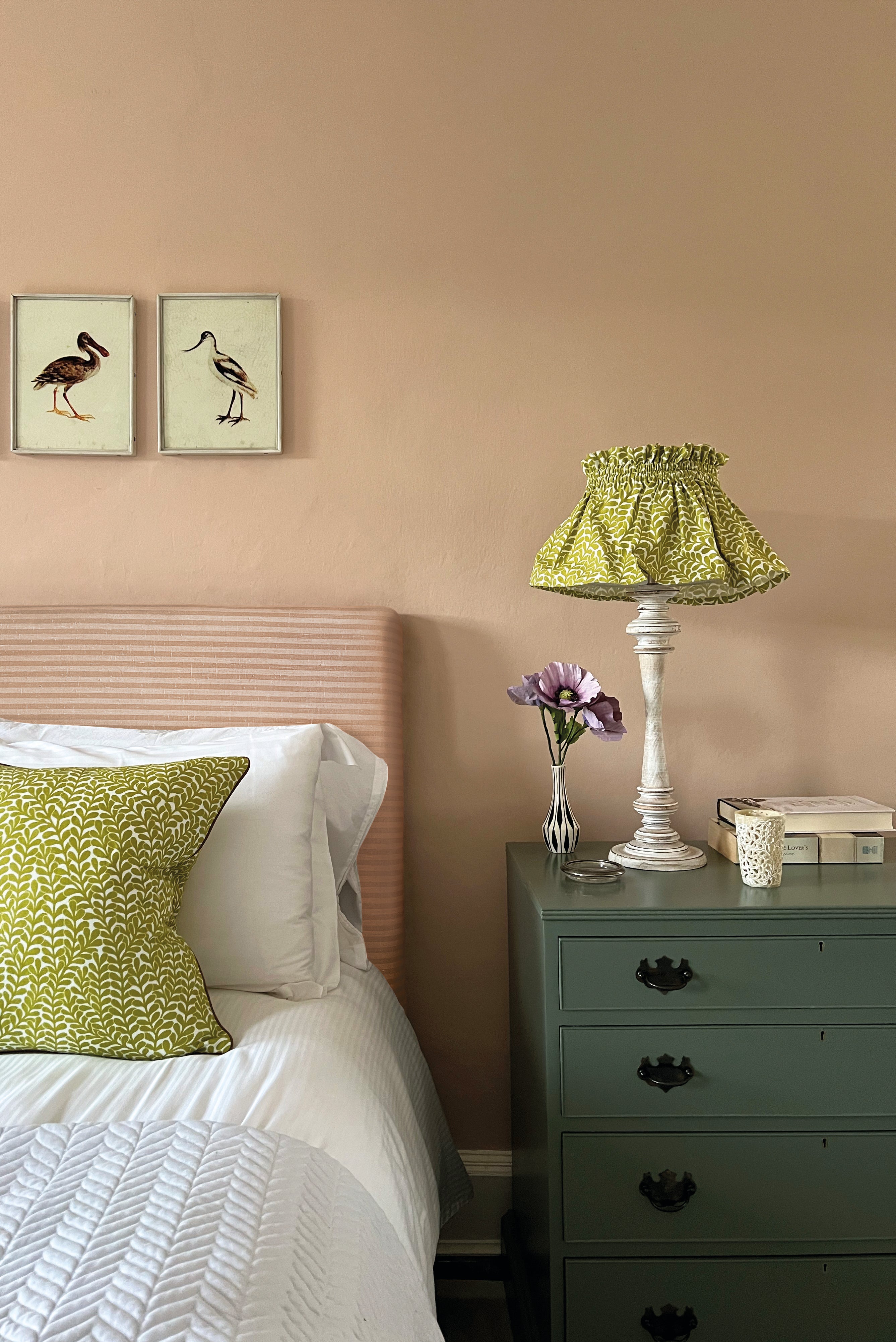A cozy bedroom tableau with a amp and throw pillows all upholstered in the same scrolling stem and leaf print.