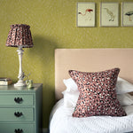 A cozy bedroom tableau with framed bird prints and a statement wall papered in a scrolling stem and leaf print.