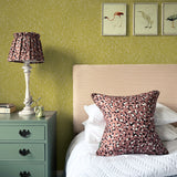 A cozy bedroom tableau with framed bird prints and a statement wall papered in a scrolling stem and leaf print.