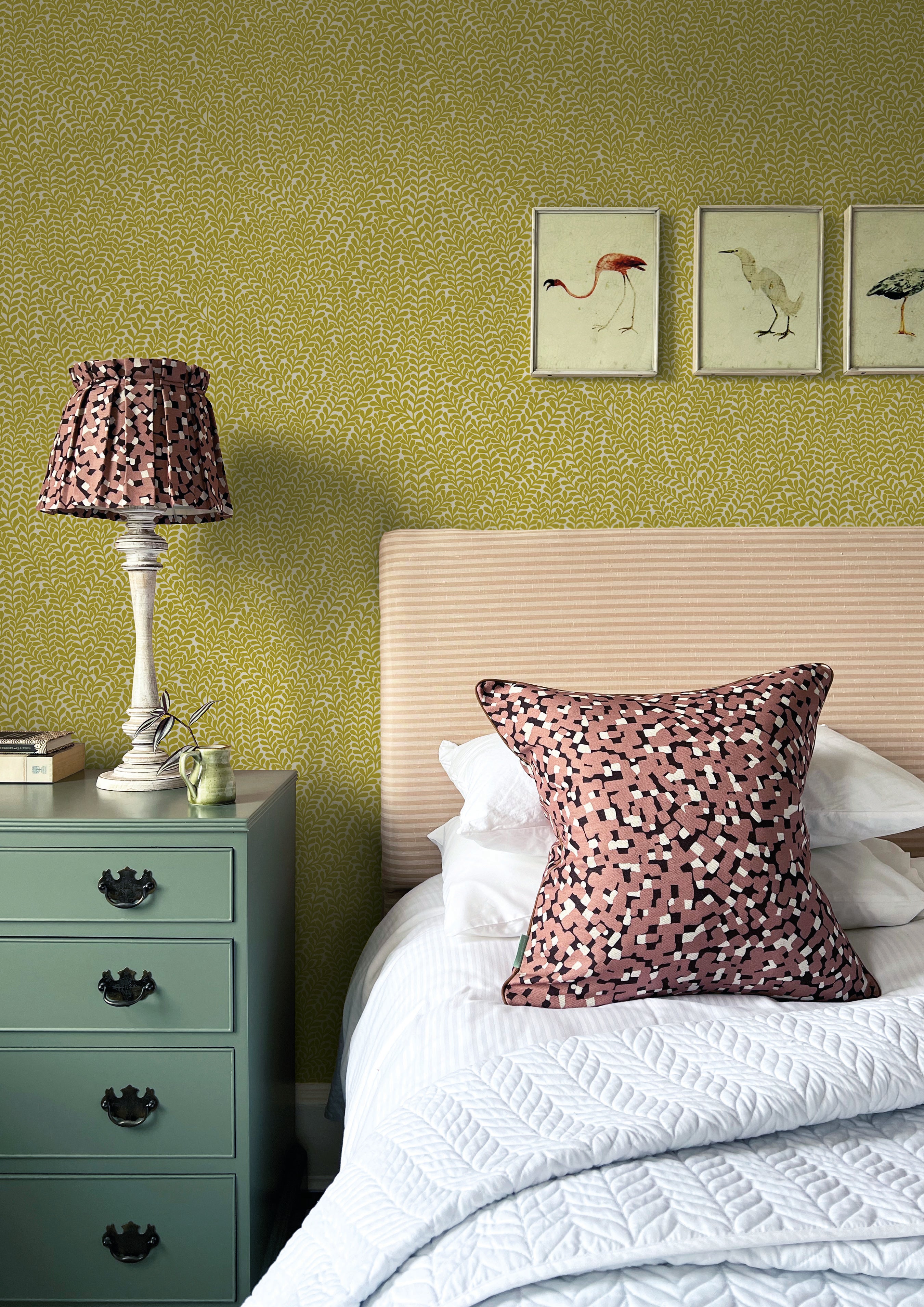 A cozy bedroom tableau with framed bird prints and a statement wall papered in a scrolling stem and leaf print.