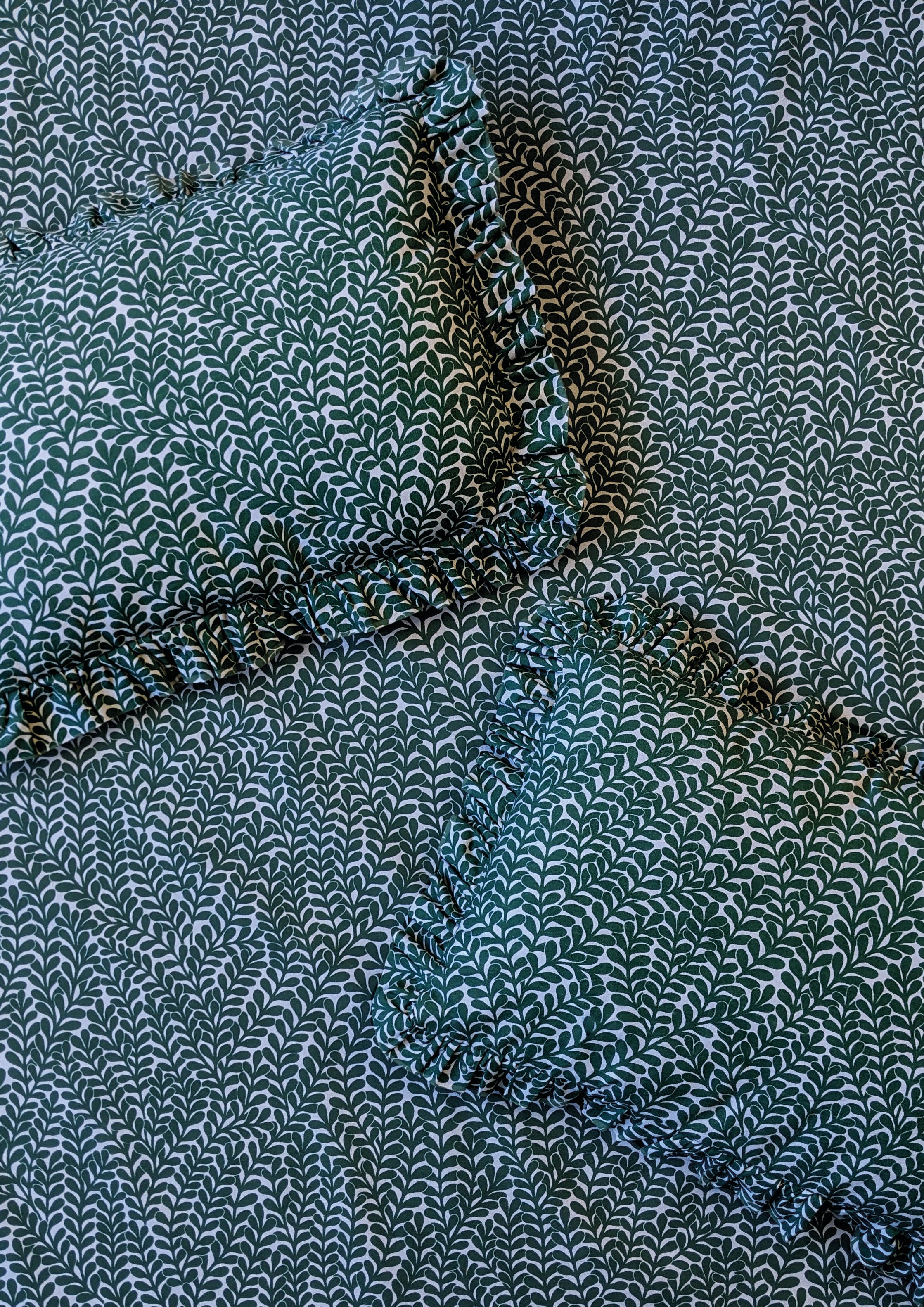 Two ruffled throw pillows lay on a fabric surface. All are upholstered in the same scrolling stem and leaf print.