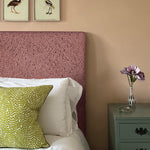 A cozy bedroom tableau with a headboard and throw pillows all upholstered in the same scrolling stem and leaf print.