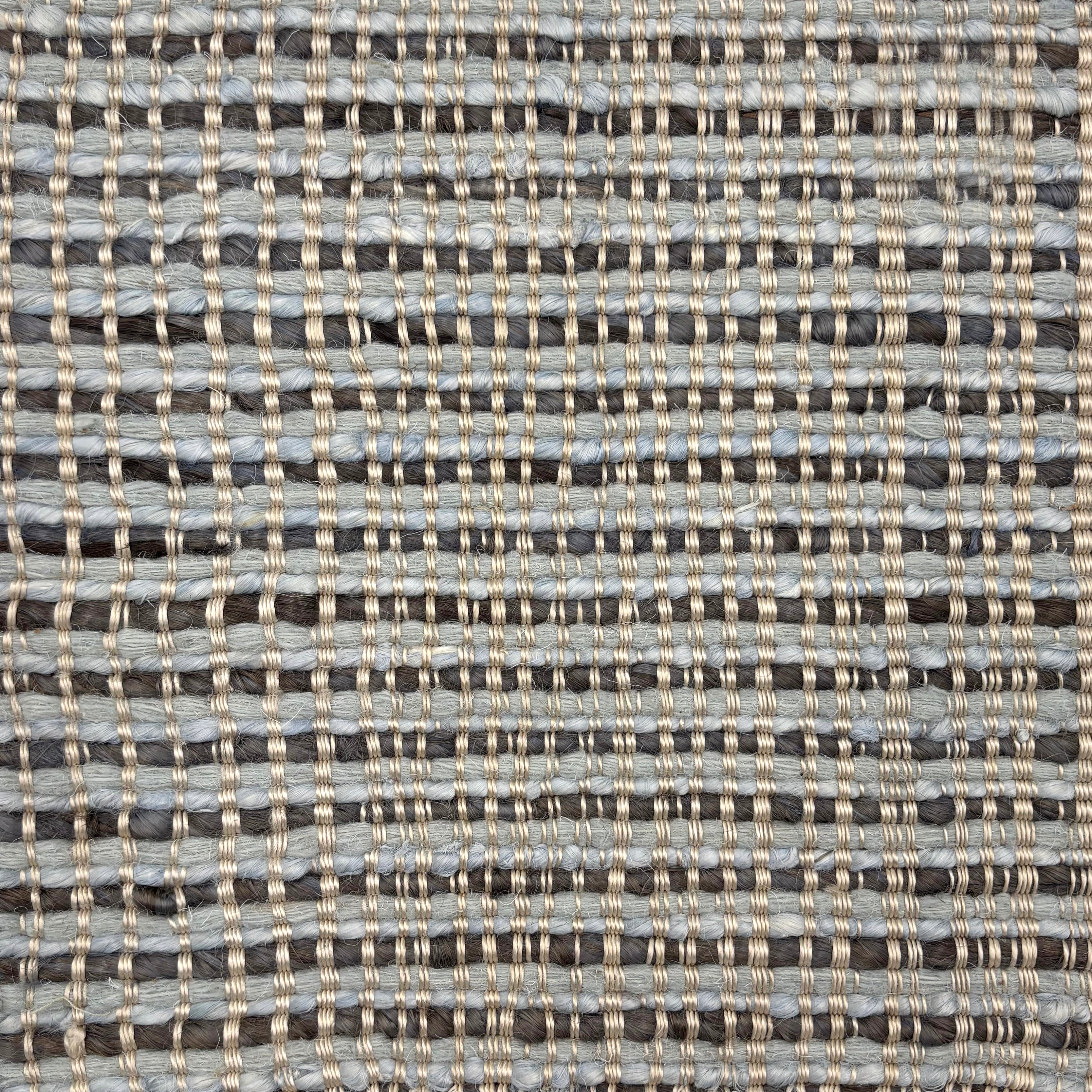 Handwoven rug with blue and charcoal stripes with a beige satin warp over top. 