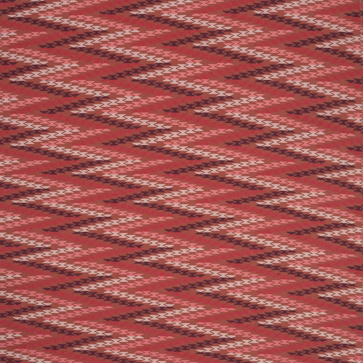 Woven fabric with geometric zig zag pattern in  shades of pink on red. 