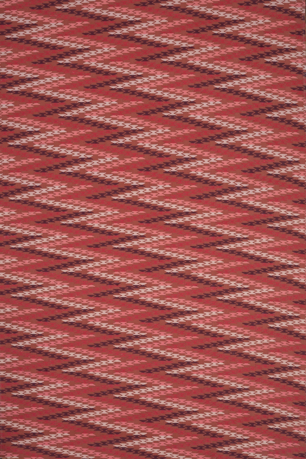 Woven fabric with geometric zig zag pattern in  shades of pink on red. 