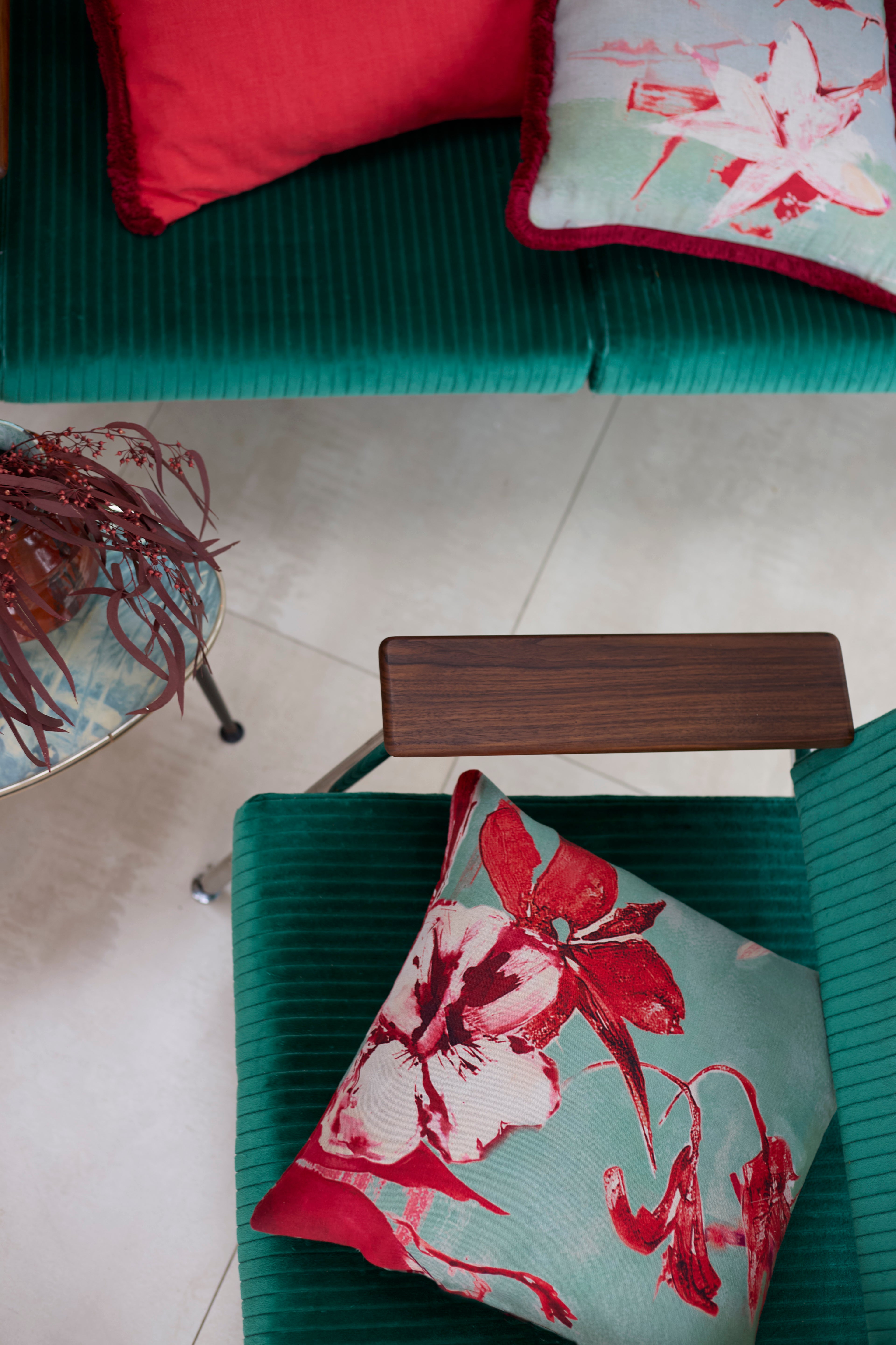 An overhead shot of teal velvet chairs with red and turquoise watercolor floral throw pillows.