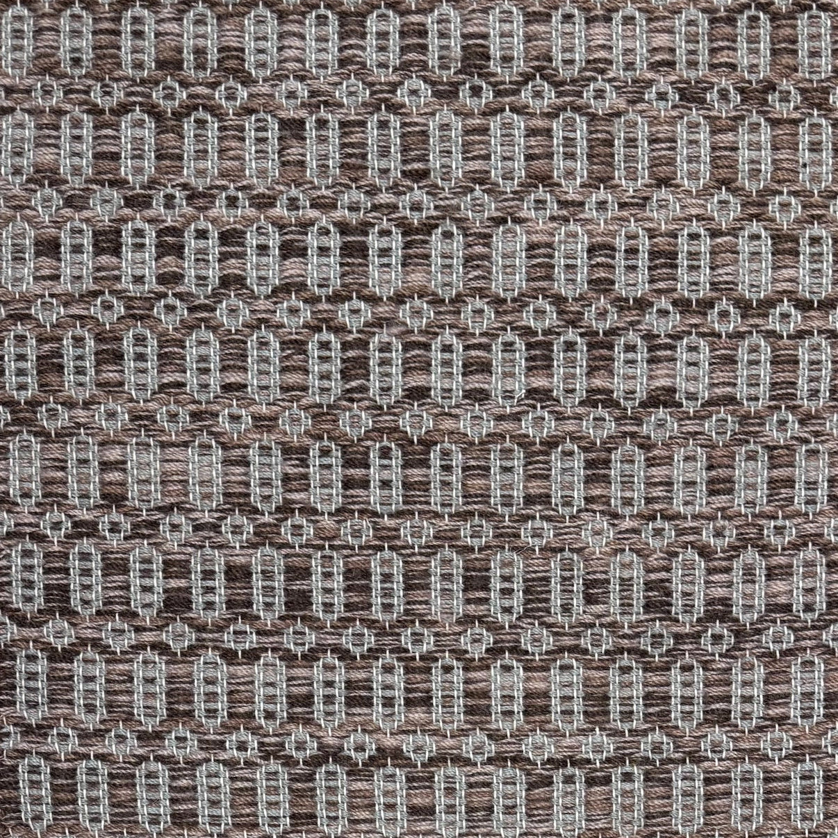 Handwoven wool rug with an oval and diamond lattice pattern in shades of brown and grey-blue. 